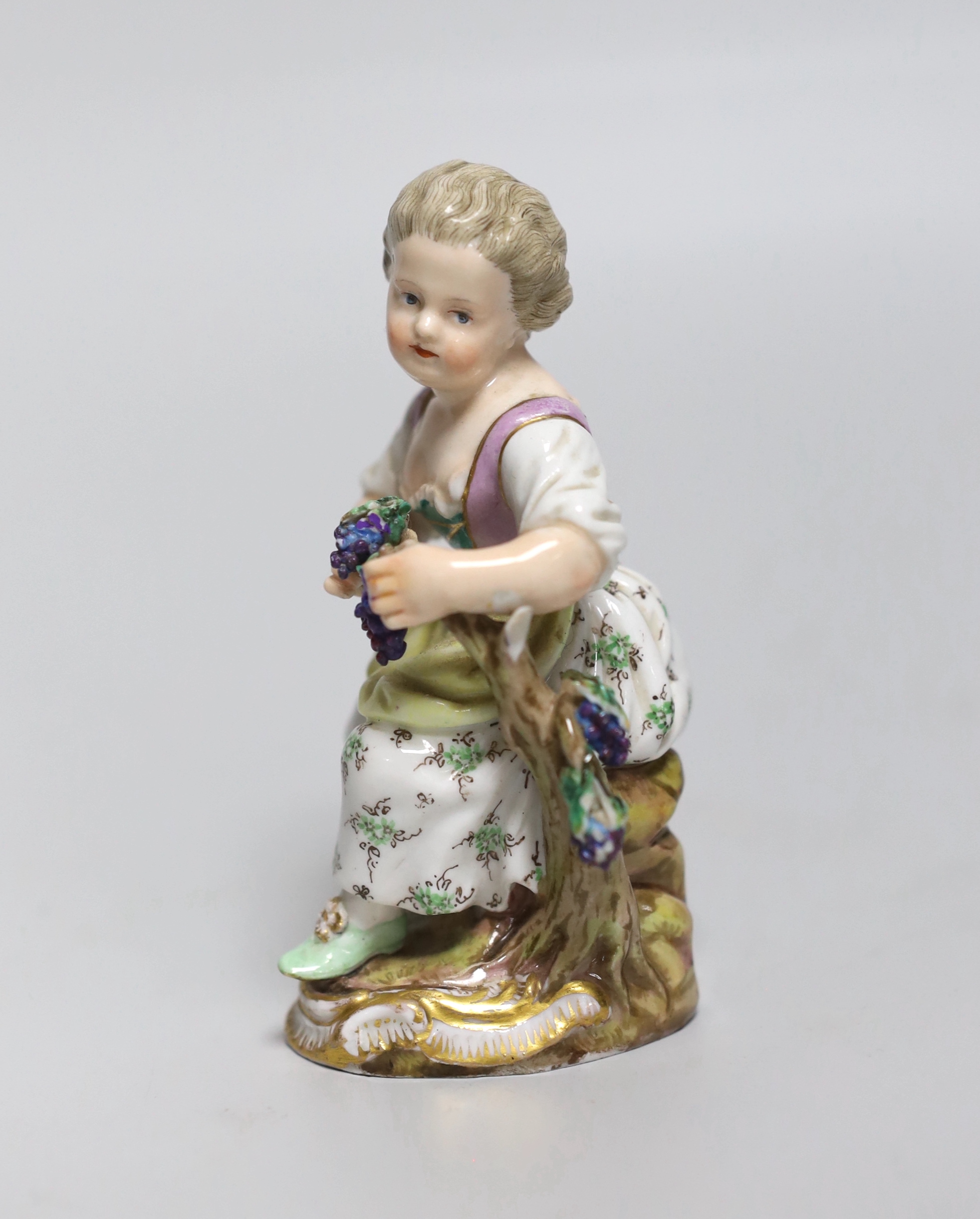 An early 19th century Meissen figure of a girl seated on a tree stump holding a bunch of grapes, painted 58, incised mark and feint crossed swords in blue, 11cm